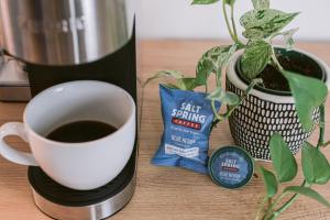 a cup of coffee next to a coffee maker and a plant at Days Inn by Wyndham Victoria On The Harbour in Victoria