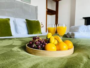 eine Schale Obst auf einem Bett mit zwei Gläsern Orangensaft in der Unterkunft Lovely 4 Bed, Family & Contractors Luton Airport & M1 by Properties2you in Luton