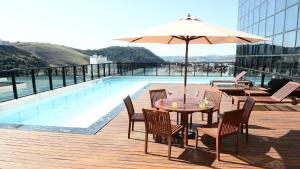 uma mesa e cadeiras com um guarda-sol ao lado de uma piscina em Trade Hotel em Juiz de Fora