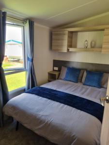 a bedroom with a bed with blue pillows and a window at Modern Family Caravan with WiFi at Valley Farm, Clacton-on-Sea in Great Clacton
