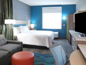 Home2 Suites By Hilton Pensacola I-10 Pine Forest Road في بينساكولا: غرفة فندقية بسرير كبير وكرسي