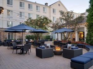 un patio esterno con tavoli, sedie e ombrelloni di Hilton Garden Inn Melville a Plainview