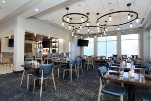 uma sala de jantar com mesas e cadeiras e um lustre em Hilton Garden Inn Melville em Plainview