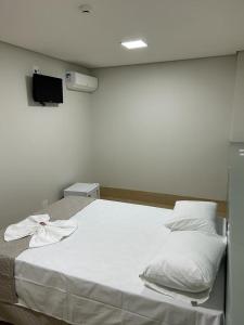 a bed with white sheets and pillows in a room at Bravo City Hotel Urupês 