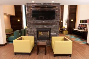 a lobby with a fireplace and two yellow chairs at Hampton Inn & Suites East Gate Regina in Regina