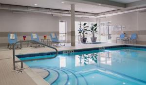 a large swimming pool with blue chairs and tables at Homewood Suites by Hilton Winnipeg Airport - Polo Park in Winnipeg
