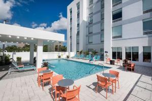a swimming pool with chairs and tables and a building at Home2 Suites By Hilton Ft. Lauderdale Airport-Cruise Port in Dania Beach