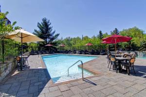 una piscina con mesas, sillas y sombrillas en Homewood Suites by Hilton Mont-Tremblant Resort en Mont-Tremblant