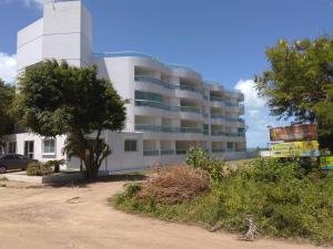 ein großes weißes Gebäude mit einem Baum davor in der Unterkunft Flat de frente ao mar in Conde