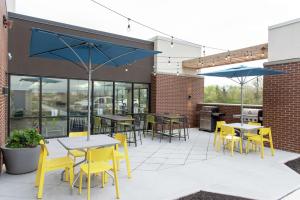 eine Terrasse mit Tischen, gelben Stühlen und Sonnenschirmen in der Unterkunft Home2 Suites By Hilton Indianapolis Airport in Indianapolis