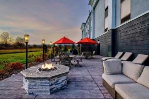 een patio met een vuurplaats en tafels en parasols bij Hampton Inn Cortland in Cortland