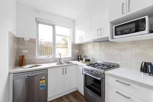 a kitchen with white cabinets and a stove and microwave at Serene Coastal Haven in Melbourne