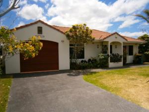 una casa bianca con garage marrone di Baskervilla - Whangamata Holiday Home a Whangamata