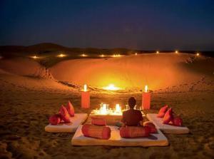 a person sitting on a bed in the sand with candles at Jaisal heritage desert camp in Jaisalmer