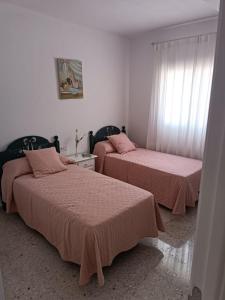 1 dormitorio con 2 camas con sábanas rosas y ventana en Casa EDU en Sanlúcar de Barrameda