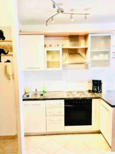 Cute and Cosy apartment في زغرب: مطبخ فيه دواليب بيضاء واجهزة سوداء