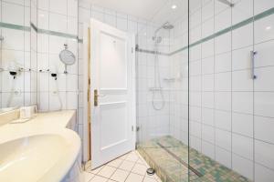 a bathroom with a tub and a glass shower door at Strandhotel Sylt Westerland in Westerland +37 photos