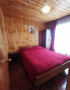 um quarto com uma cama vermelha num quarto de madeira em Cabañas amobladas en salto del laja a 2 minutos del puente salto del laja em El Manzano
