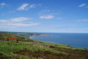 un banco sentado en la cima de una colina con vistas al océano en Smugglers Rock Cottages, en Ravenscar