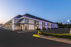 Days Inn & Suites by Wyndham Fort Bragg/Cross Creek Mall في فايتفيل: مبنى كبير مع إضاءة أرجوانية في موقف للسيارات