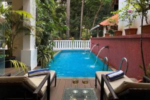 a swimming pool in a yard with chairs and a table at StayVista at Villa Arcadia with Alfresco Dining in Candolim