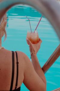 a woman in a bikini holding a drink in front of a pool at Anemos Inn by Estia in Kokkíni Khánion