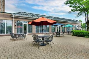 un patio con tavoli, sedie e ombrellone di Hilton Garden Inn Louisville Airport a Louisville