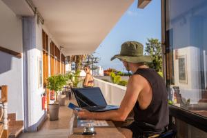 a man with a hat sitting at a table with a laptop at Ocean Nomads Coworking in Arona