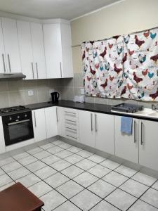 a kitchen with white cabinets and a curtain with chickens on it at Despatch Self Catering Apartments in Despatch