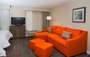 un salon avec un canapé orange et une télévision dans l'établissement Hampton Inn & Suites Valdosta/Conference Center, à Valdosta