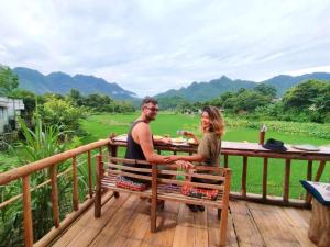 a man and woman sitting on a bench on a deck at Meadow Mai Chau Homestay in Mai Châu