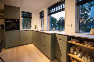 a large kitchen with green cabinets and windows at B&B de oude melkfabriek in Valkenswaard