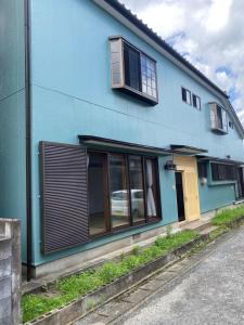 un edificio azul con una puerta y ventanas amarillas en 民泊　筑紫野 en Chikushino