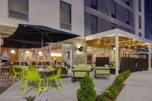 un patio avec des chaises vertes, des tables et des parasols dans l'établissement Home2 Suites By Hilton Nashville Downtown-Metrocenter, à Nashville