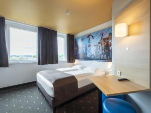 a hotel room with a bed and a desk and windows at B&B Hotel Landshut in Landshut