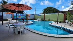 a pool with a table and chairs and an umbrella at Hotel Enseada dos Corais in Cabo de Santo Agostinho