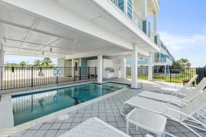 a swimming pool with white chairs next to a building at St Joe Beach House - Sailfish by Panhandle Getaways in Saint Joe Beach