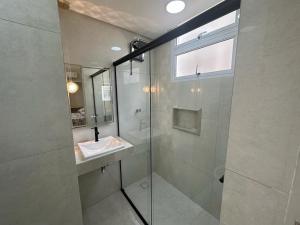 uma casa de banho com uma cabina de duche em vidro e um lavatório. em Refúgio Costeiro no Guarujá
