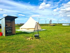 ein weißes Zelt auf einem Feld neben einem Gebäude in der Unterkunft Boyce Fen Farm Retreat Glamping & Fishery in Wisbech