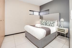 a white bedroom with a large bed and a side table at Urban Oasis Apartments at The Vantage in Johannesburg