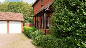 a brick house with a garage and a large bush at The Cosy Corner in Loughton