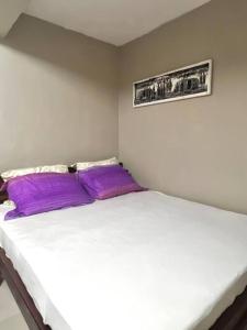 Cozy studio apartment في دار السلام: سرير أبيض مع وسائد أرجوانية في الغرفة