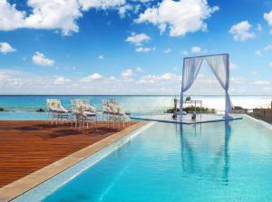 a swimming pool with chairs and a table and the ocean at The Fives Downtown Hotel & Residences, Curio Collection by Hilton in Playa del Carmen
