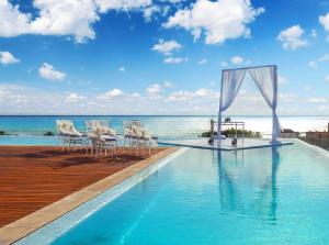 una piscina con sillas, una mesa y el océano en The Fives Downtown Hotel & Residences, Curio Collection by Hilton en Playa del Carmen