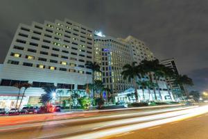 Hilton Colon Guayaquil Hotel في غواياكيل: شارع المدينة فيه مباني والنخيل بالليل