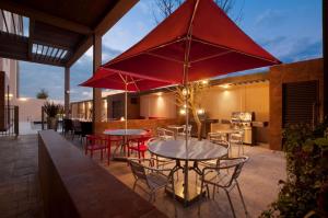 un patio avec des tables, des chaises et des parasols rouges dans l'établissement Homewood Suites by Hilton Queretaro, à Querétaro