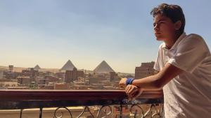 a young man standing on a balcony looking at the pyramids at Key of pyramids view inn in Cairo