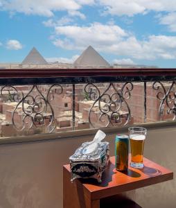 a table with a glass of beer on a balcony with the pyramids at Key of pyramids view inn in Cairo