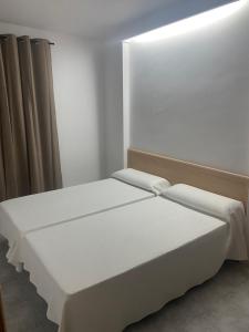 Cama en habitación con paredes y cortinas blancas en Hostal Concepción, en La Mata