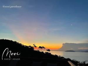 a sunset over the ocean with palm trees on a hill at Mooi Guest House in Ilhabela